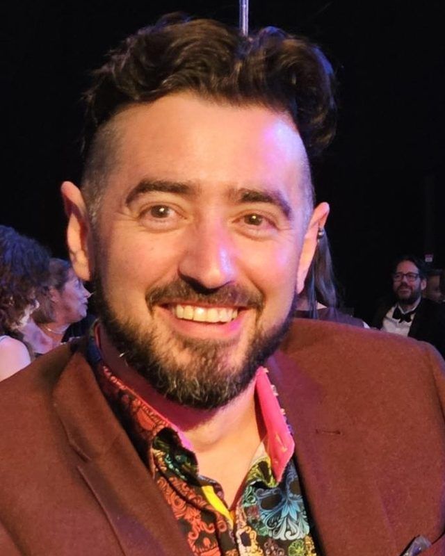 Steven Burton smiling, wearing a rust-brown blazer over a colourfully patterned shirt